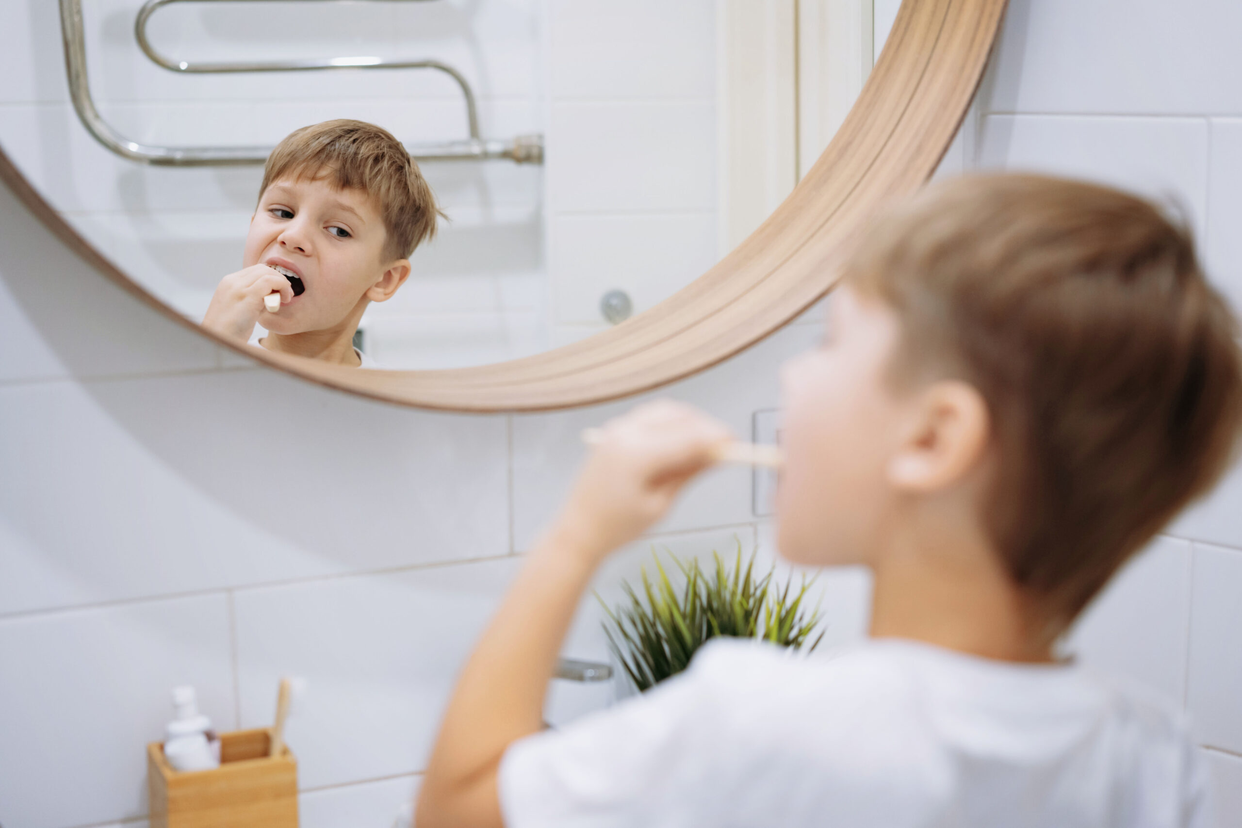 boy brushing teeth with bamboo tooth brush in bathroom looking into mirror